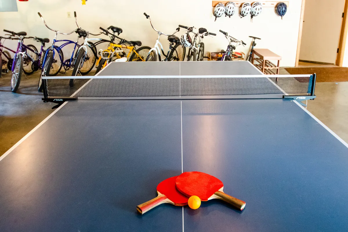 A lively interior shot with a ping pong table in the foreground and several bicycles stored at the back. The space is energetic, hinting at family bonding, friendly competitions, and easy access to bikes for adventures.