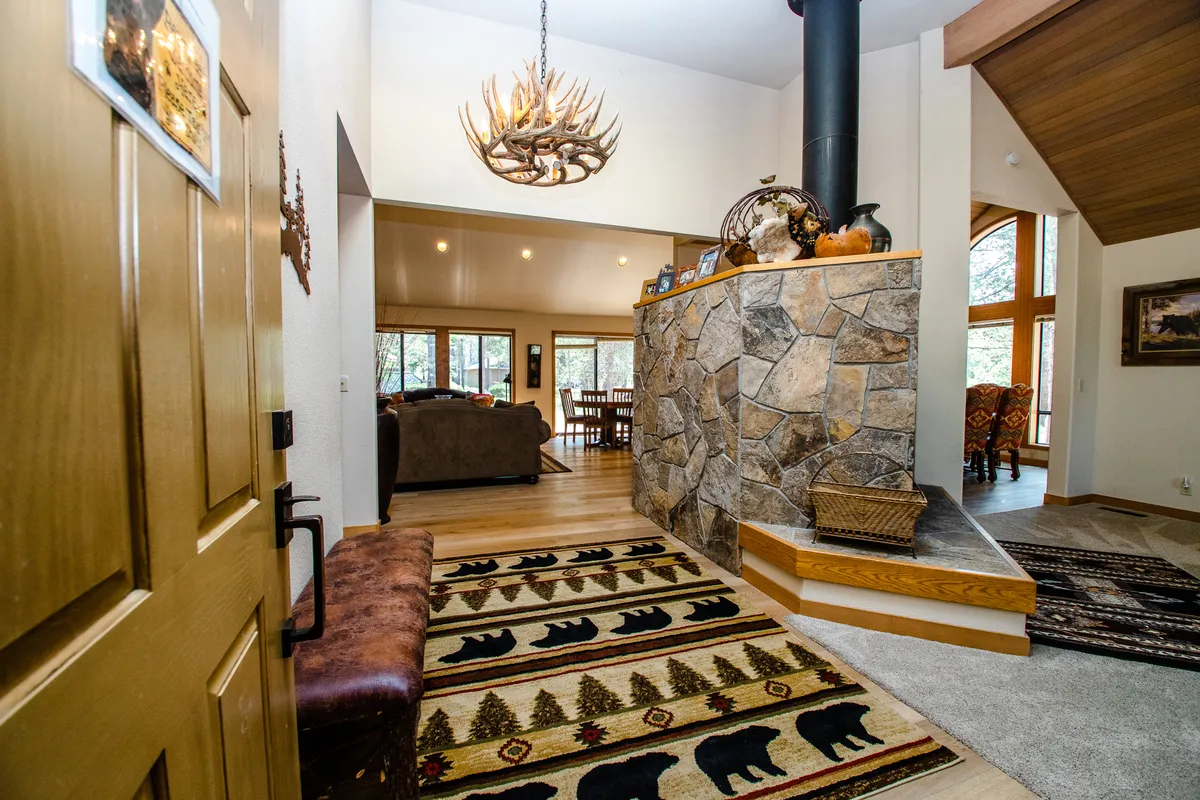 A rustic, inviting space centered around a striking stone fireplace, with an antler chandelier overhead and a decorative bear rug adding a playful mountain touch. The wooden bench and soft lighting make the area perfect for fireside chats or unwinding after a day of adventure.