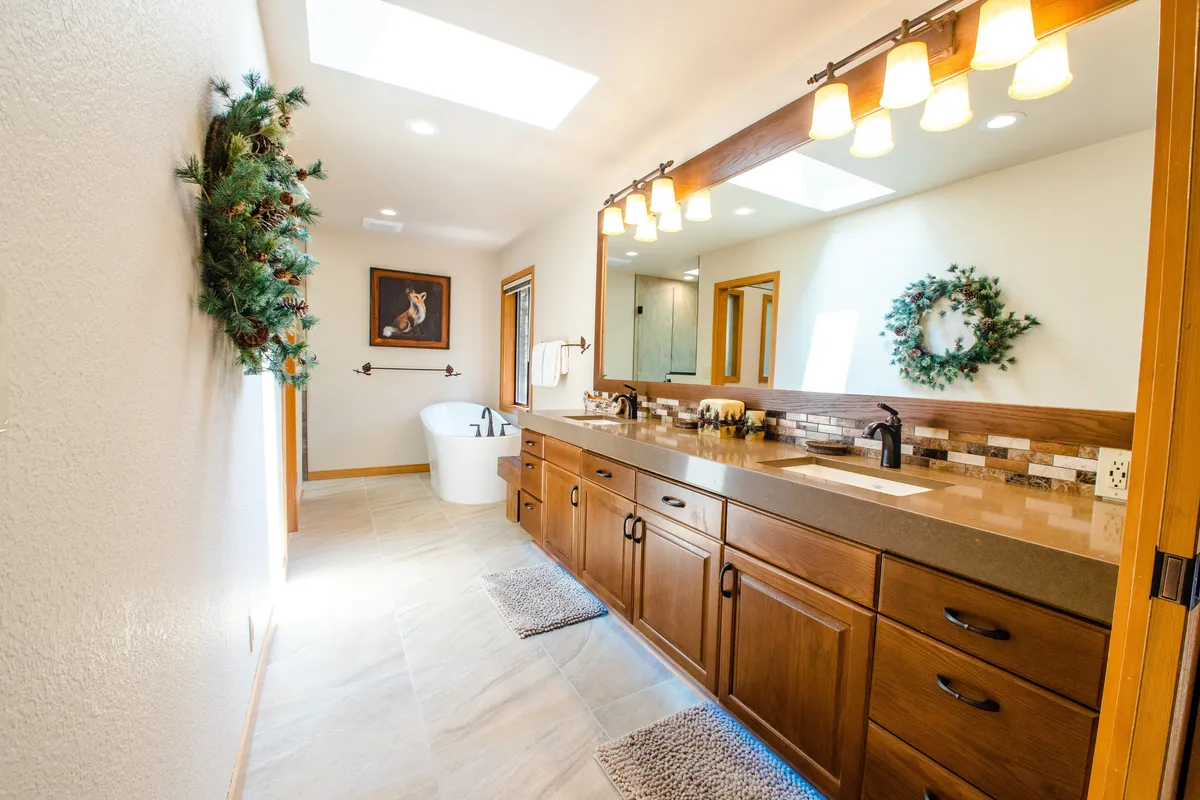 A spa-like bathroom with a freestanding soaking tub, double sink vanity, decorative mirror, and skylights. The space is bathed in natural light, emphasizing a serene and rejuvenating ambiance ideal for relaxation and self-care.