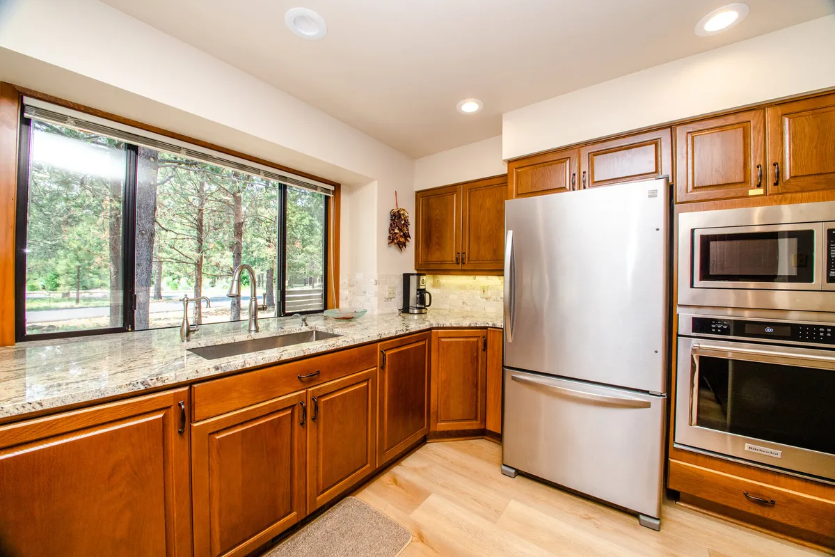 A beautifully remodeled kitchen featuring sleek granite countertops, modern appliances, and a large window that floods the space with natural light. The kitchen is warm and inviting, with refinished wood cabinets and ample workspace for meal preparation and socializing.