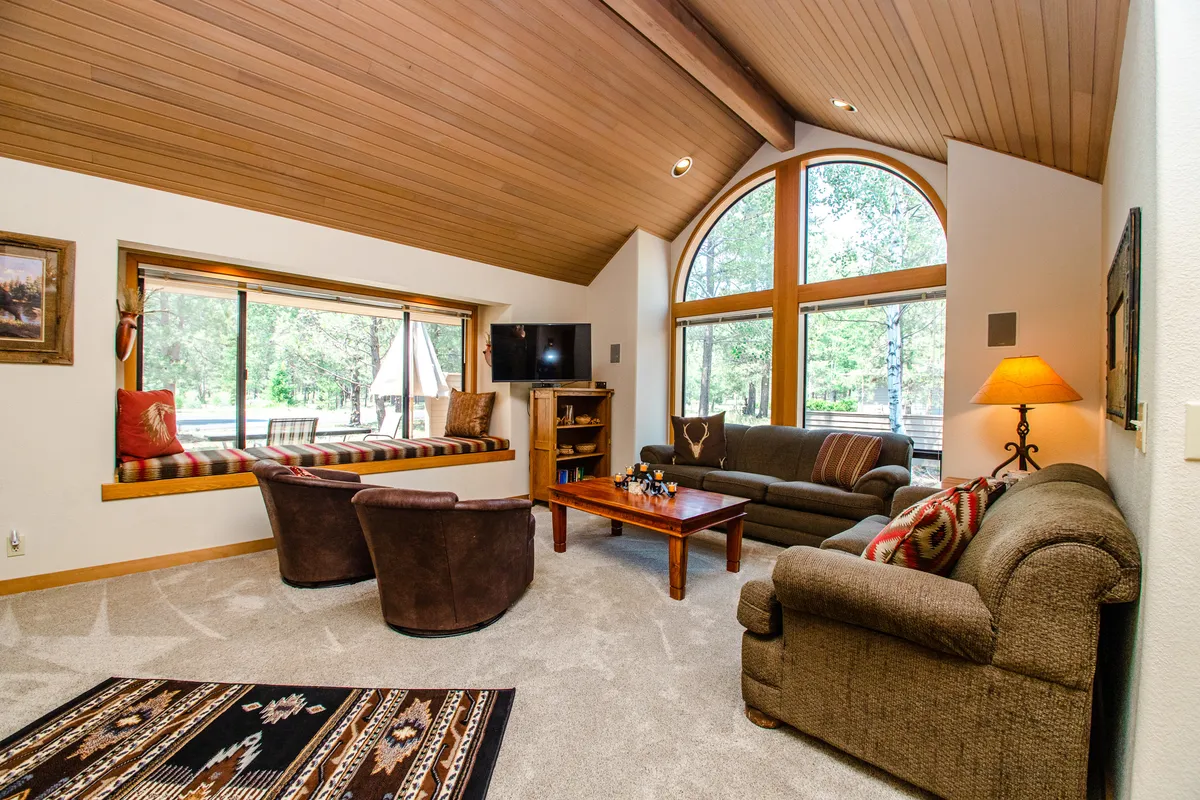 A warm and inviting living room featuring comfortable seating, a wooden coffee table set for games or conversation, and large windows offering beautiful outdoor views. Decorative pillows and subtle touches add to the relaxed, homey feel, with the fireplace adding a sense of coziness.