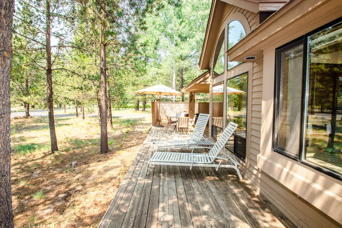 The photo features a deck with lounge chairs, a dining set, sun umbrellas, and lush forest surroundings. It evokes a sense of leisurely outdoor living and showcases the perfect spot for meals, relaxing, or recounting the day’s adventures.