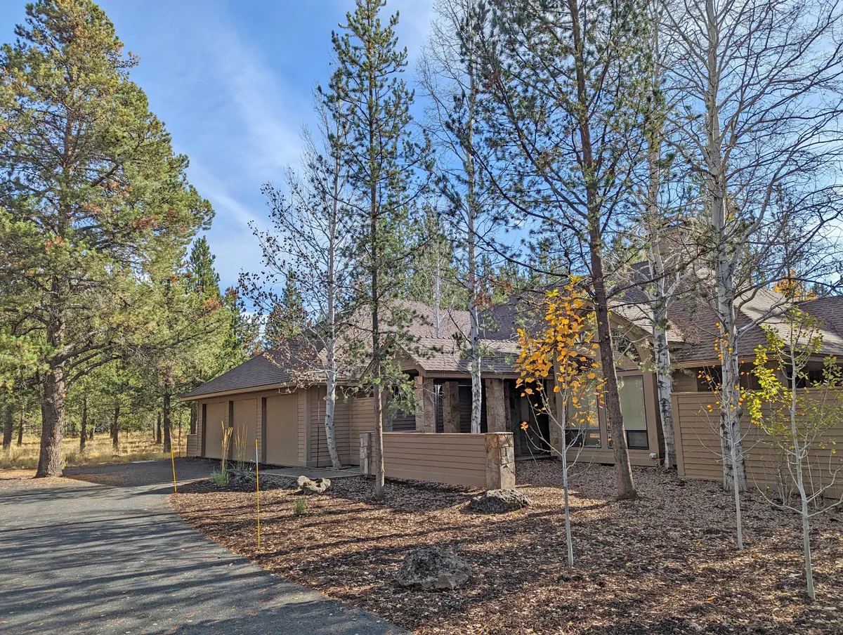 This exterior image features the main entrance of the home, surrounded by tall trees and a spacious driveway. The setting is tranquil, with natural landscaping and an inviting porch area that hints at outdoor relaxation and easy access to nature.
