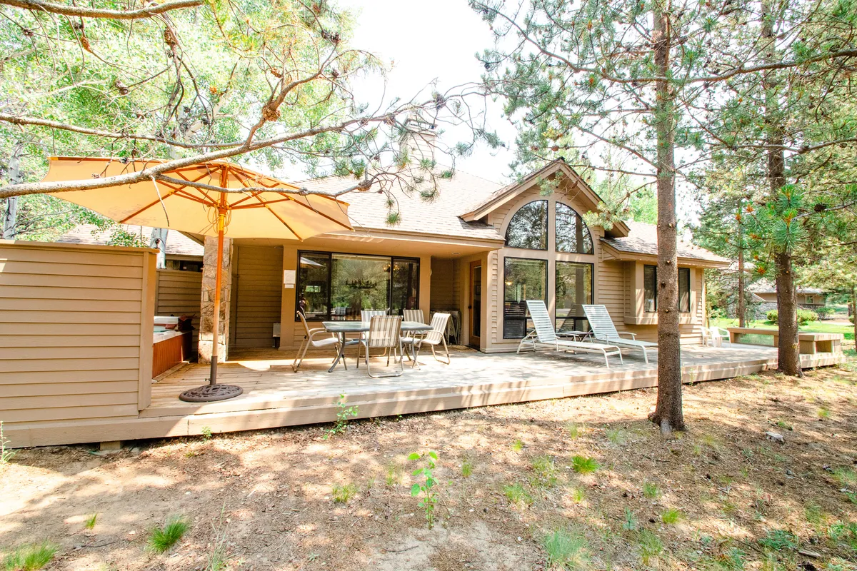 An inviting shot of the home's deck area featuring comfortable outdoor seating, a large umbrella for shade, and broad windows looking into the house. The scene suggests both relaxation and sociability, with the deck positioned for sunbathing, morning coffee, or evening gatherings.